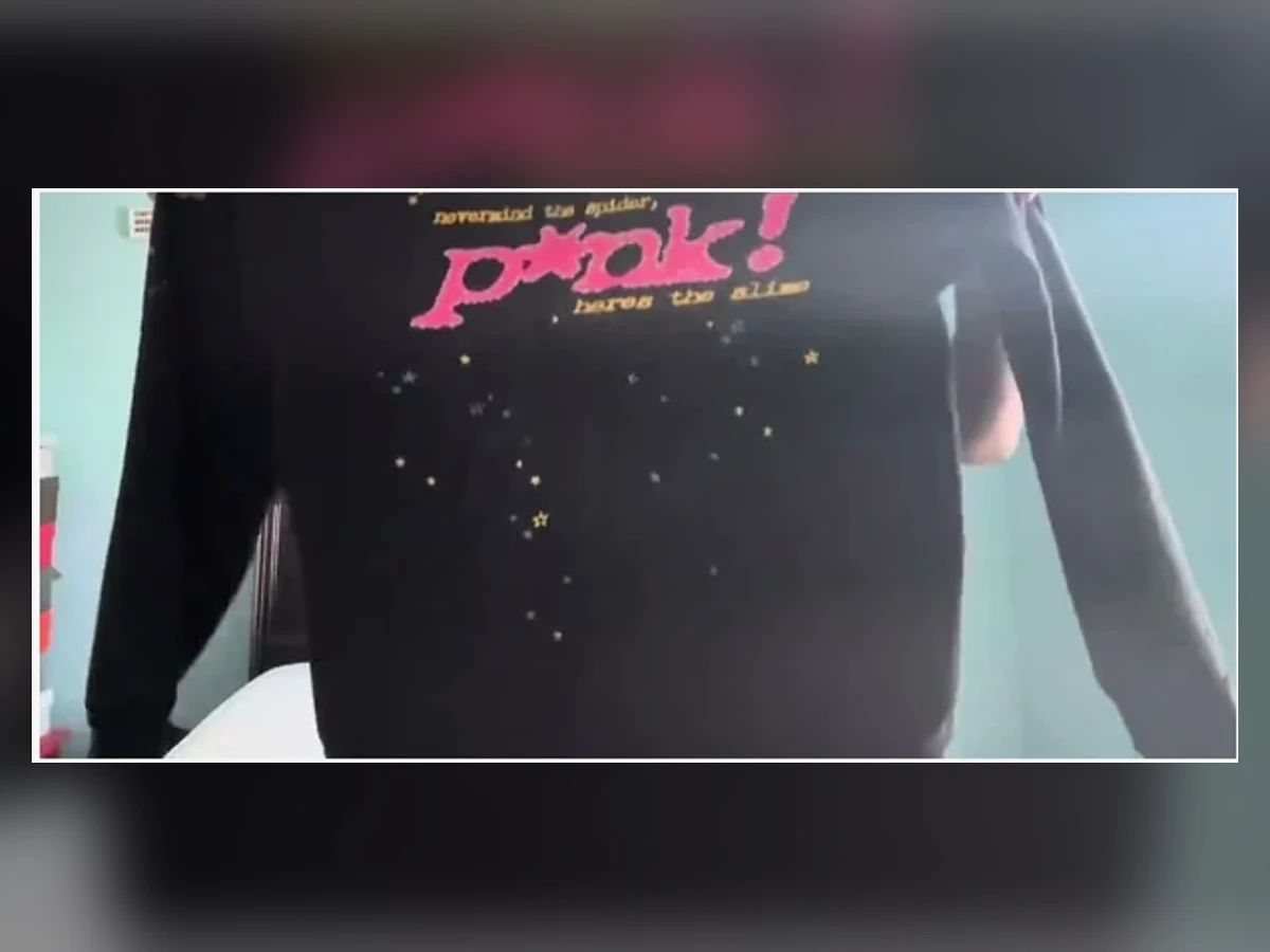 Close-up of the exact black and pink Sp5der rhinestone hoodie held in front of the camera