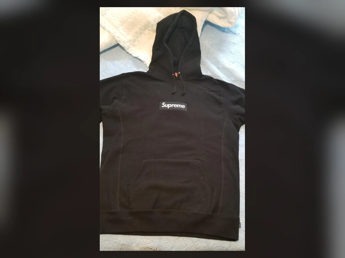 Exact black Supreme box logo hoodie laid flat on a bed
